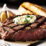 a beautifully seared steak with a golden crust, adorned with a pat of melting garlic butter.